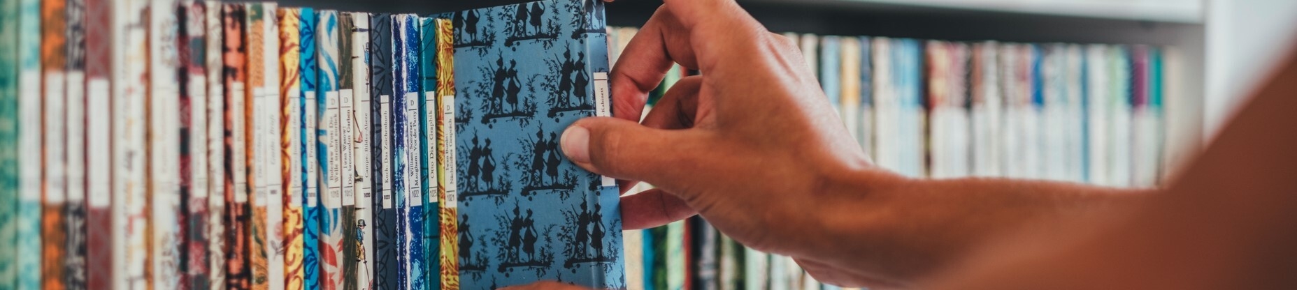 Eine Hand einer Person holt ein Buch aus einem Regal der Media-Campus-Bibliothek.