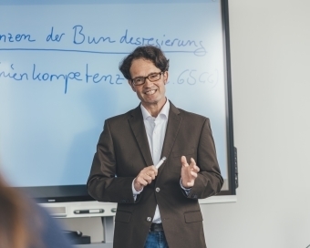 Eine Person hält vor einem White Board einen Vortrag.