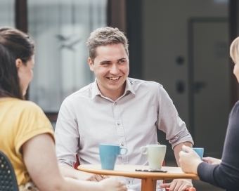 Drei Personen sitzen gemeinsam an einem Tisch und unterhalten sich bei einem Getränk.