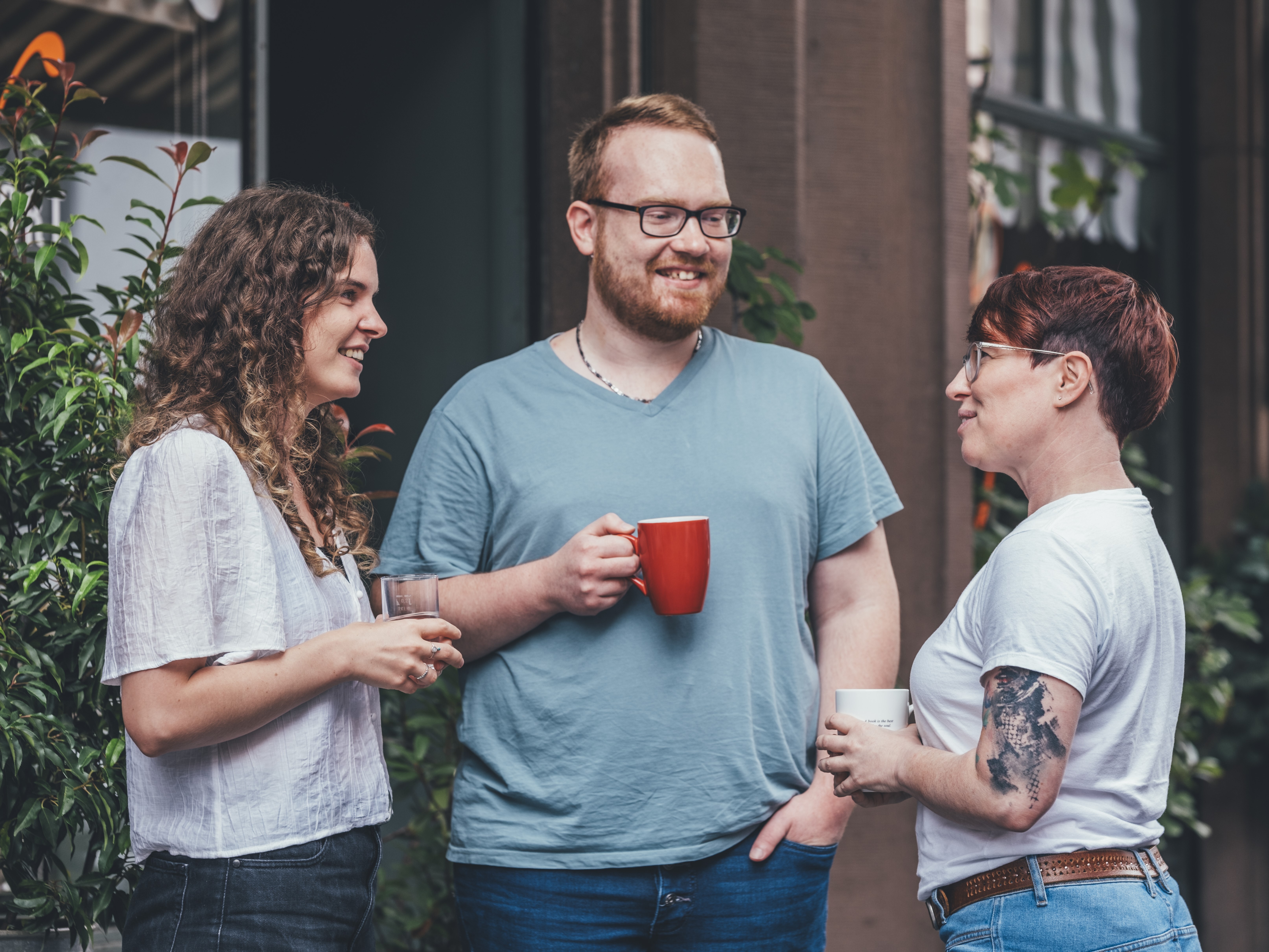 Drei Personen stehen draußen vor dem Haus des Buches und unterhalten sich bei einem Kaffee.